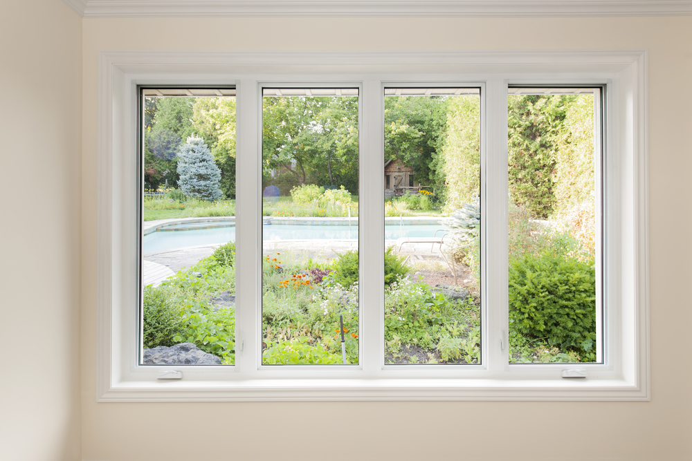 A four-panel window with a view of a summer backyard.