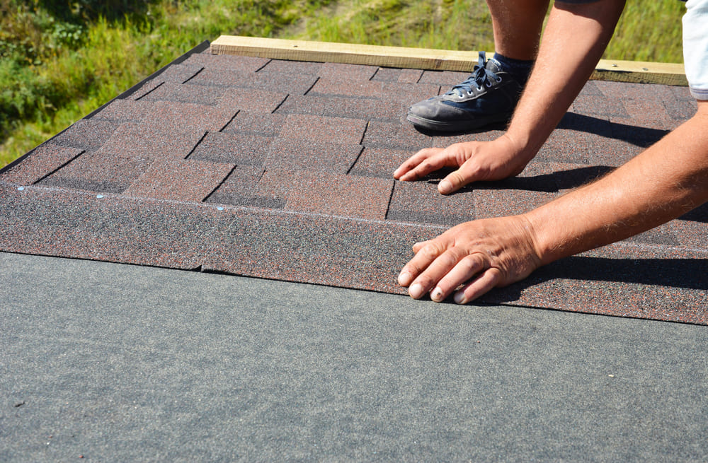 a contractor laying shingles on top of the underlayment of a roof