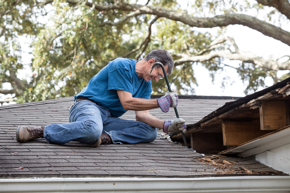 A man uses a crowbar to fix a roof that has rotten wood.