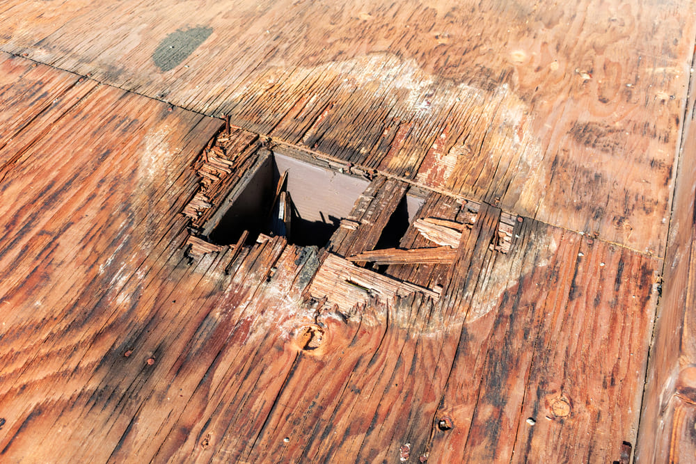 A close-up of roof decking that has rotted, with a large hole and water damage.