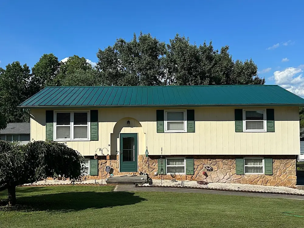 Completed metal roof replacement on a cream house with stone skirting in Powell, TN