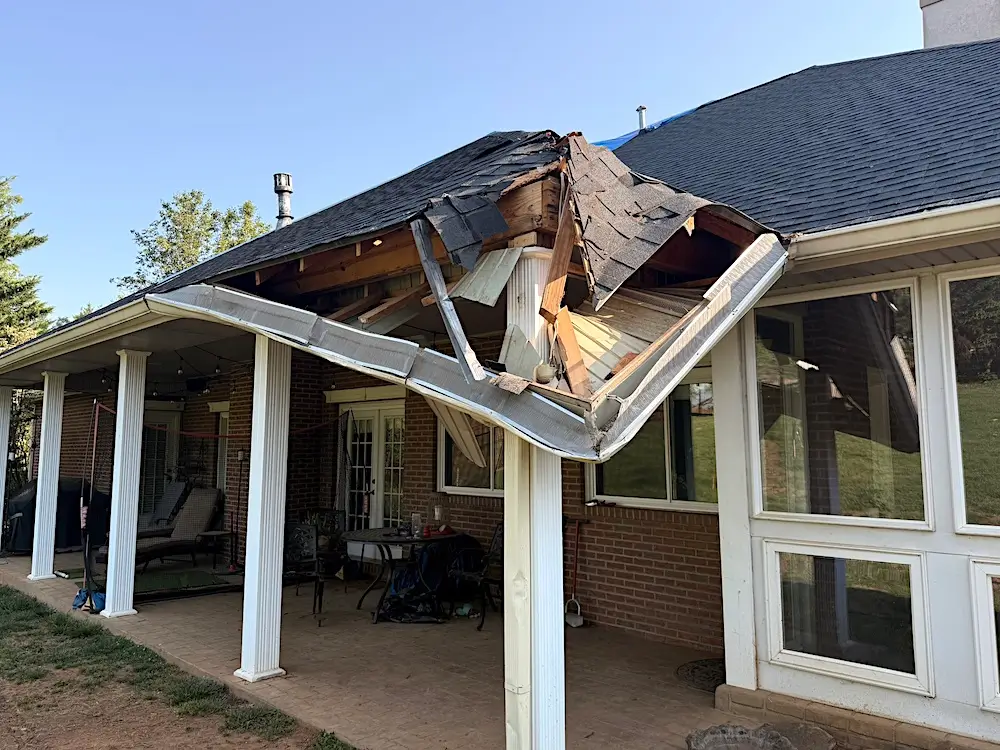 Storm-damaged rear patio roof on a brick home in Powell Tennessee showing collapsed framing, hanging shingles and a tarped main roof
